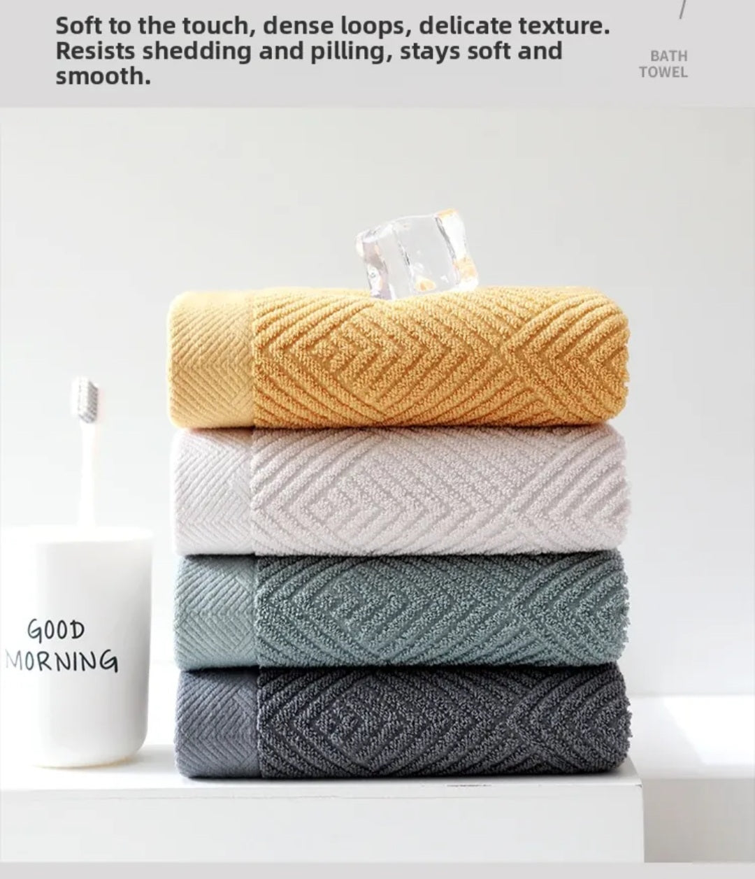 Stack of four folded cotton hand towels in mustard yellow, white, sage green and dark gray with jacquard rhombus weave