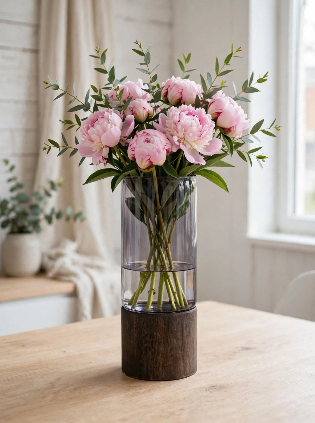 Smoky smooth glass vase on wooden base styled with pink peonies and eucalyptus