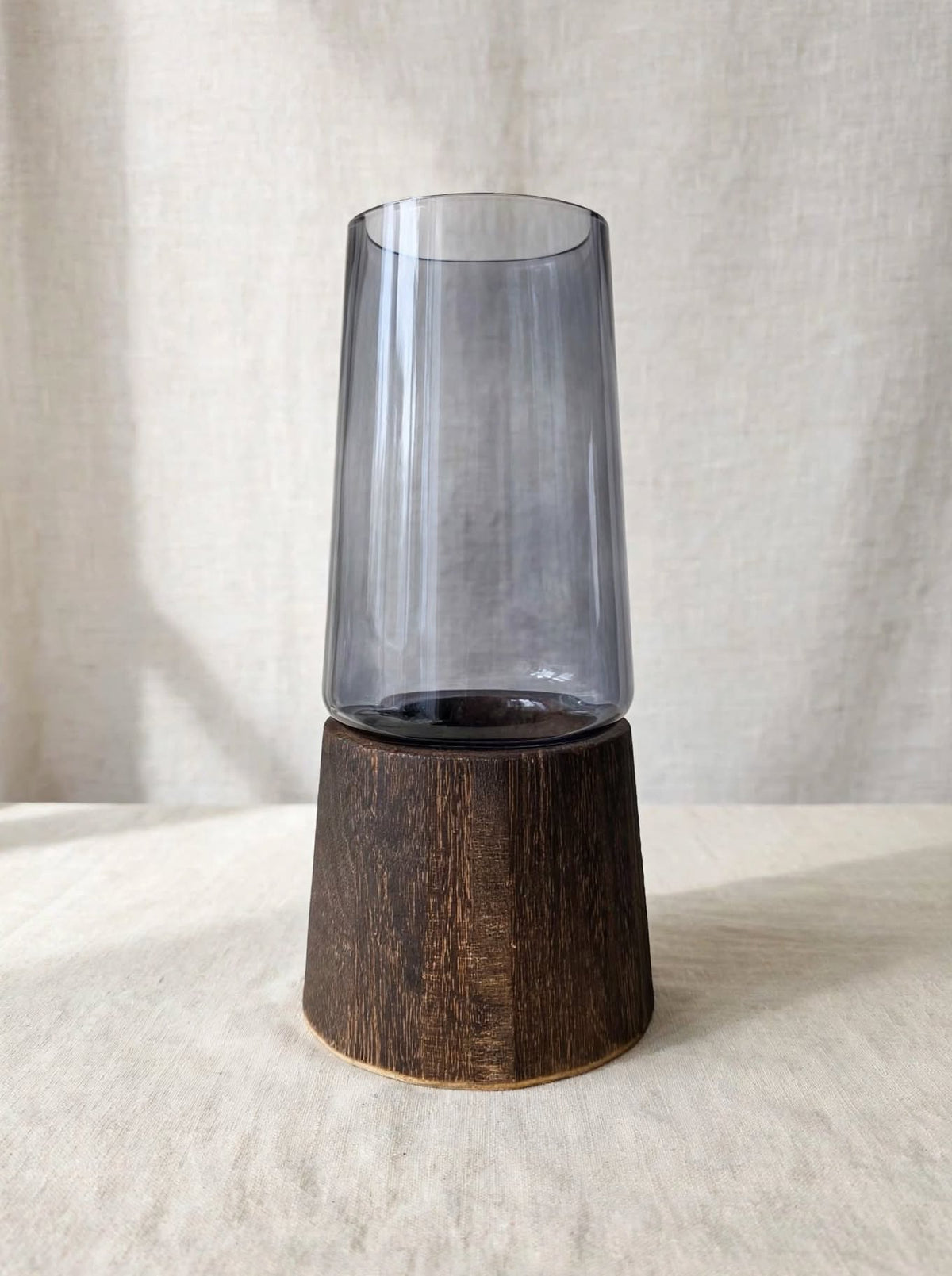 Light smoky grey glass vase on a dark wooden base, studio shot