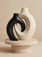 Black and white interlocking hollow-circle ceramic vases on a travertine pedestal