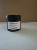 A handpoured soy candle in a dark amber glass jar with a black lid and a white label, set against a plain brown background on a light gray surface.