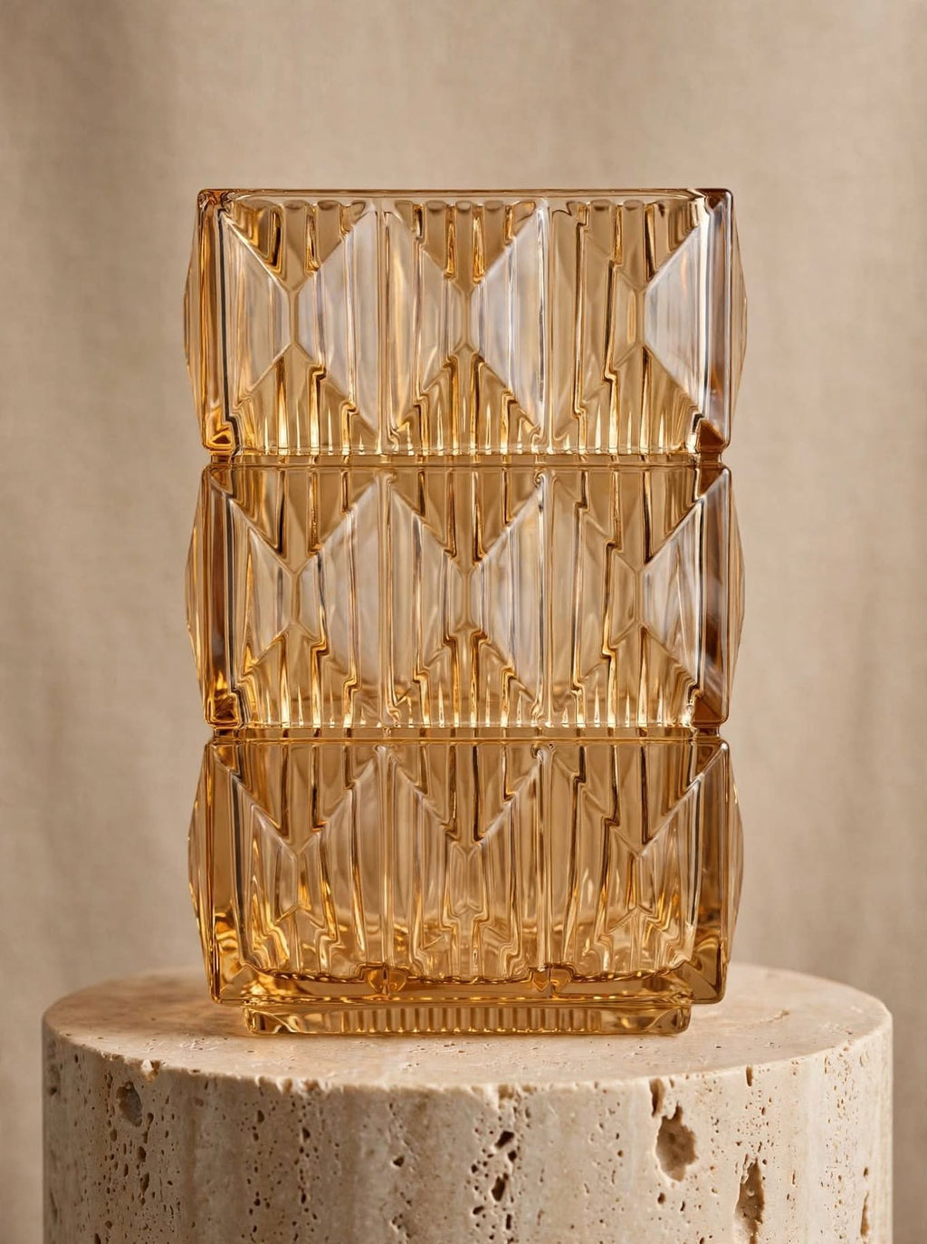 Amber square glass vase with geometric ice-crackle texture displayed on a travertine pedestal