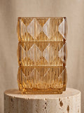 Amber square glass vase with geometric ice-crackle texture displayed on a travertine pedestal