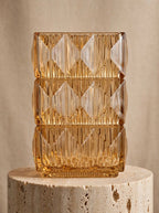 Amber square glass vase with geometric ice-crackle texture displayed on a travertine pedestal