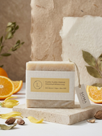 A rectangular bar of soap labeled 'Tiang Tang Orange' by Soma, styled on a stone slab with orange slices, leaves, and nuts against a warm neutral background.
