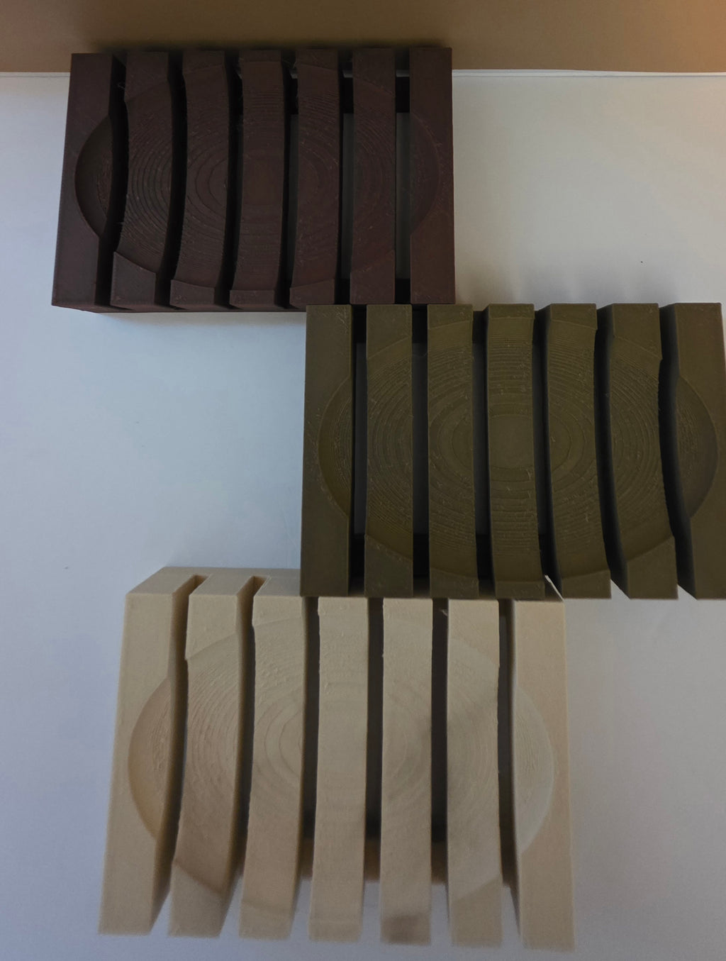 Three sets of wooden blocks with circular grooves, shown in dark brown, olive green, and light natural wood finishes on a plain white background.