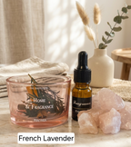 A home fragrance product setup on a tabletop with a pink glass oil diffuser bowl, a small amber dropper bottle labeled 'Fragrance', and pink crystal rocks. A beige vase with dried stems sits in the background, and a text label at the bottom reads 'French Lavender'.