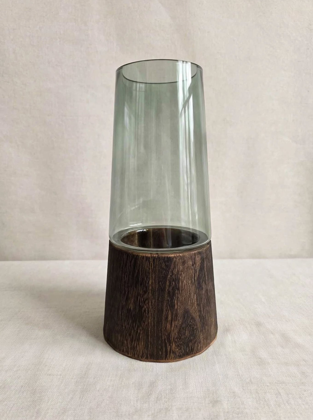Smoky green glass vase on a dark wooden base, studio shot