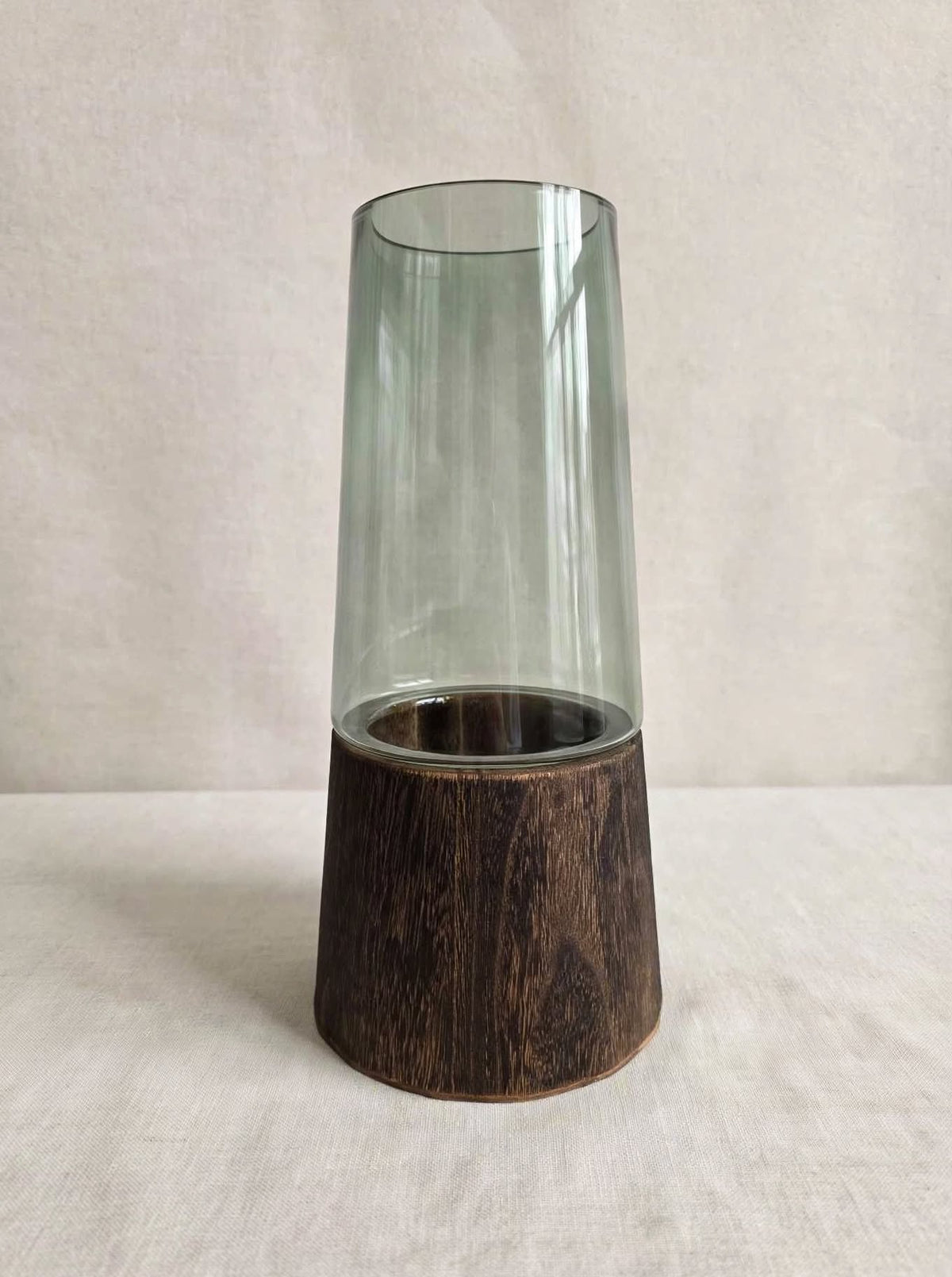 Smoky green glass vase on a dark wooden base, studio shot