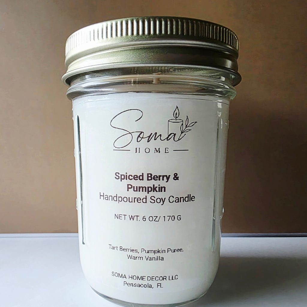 A handpoured soy candle in a clear glass mason jar with a white label and a silver metal lid, photographed against a plain brown background.
