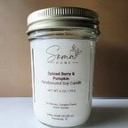 A handpoured soy candle in a clear glass mason jar with a white label and a silver metal lid, photographed against a plain brown background.