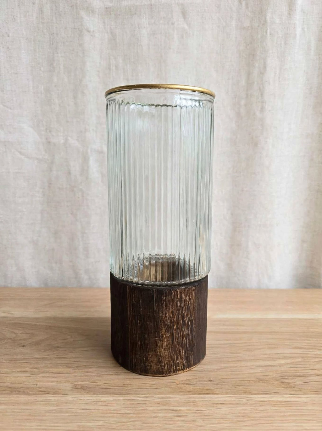 Clear ribbed glass vase with gold rim on a wooden base, studio shot