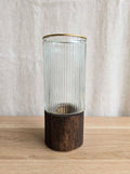 Clear ribbed glass vase with gold rim on a wooden base, studio shot