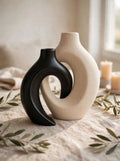 Black and white interlocking ceramic donut vases styled on linen with olive sprigs and candles
