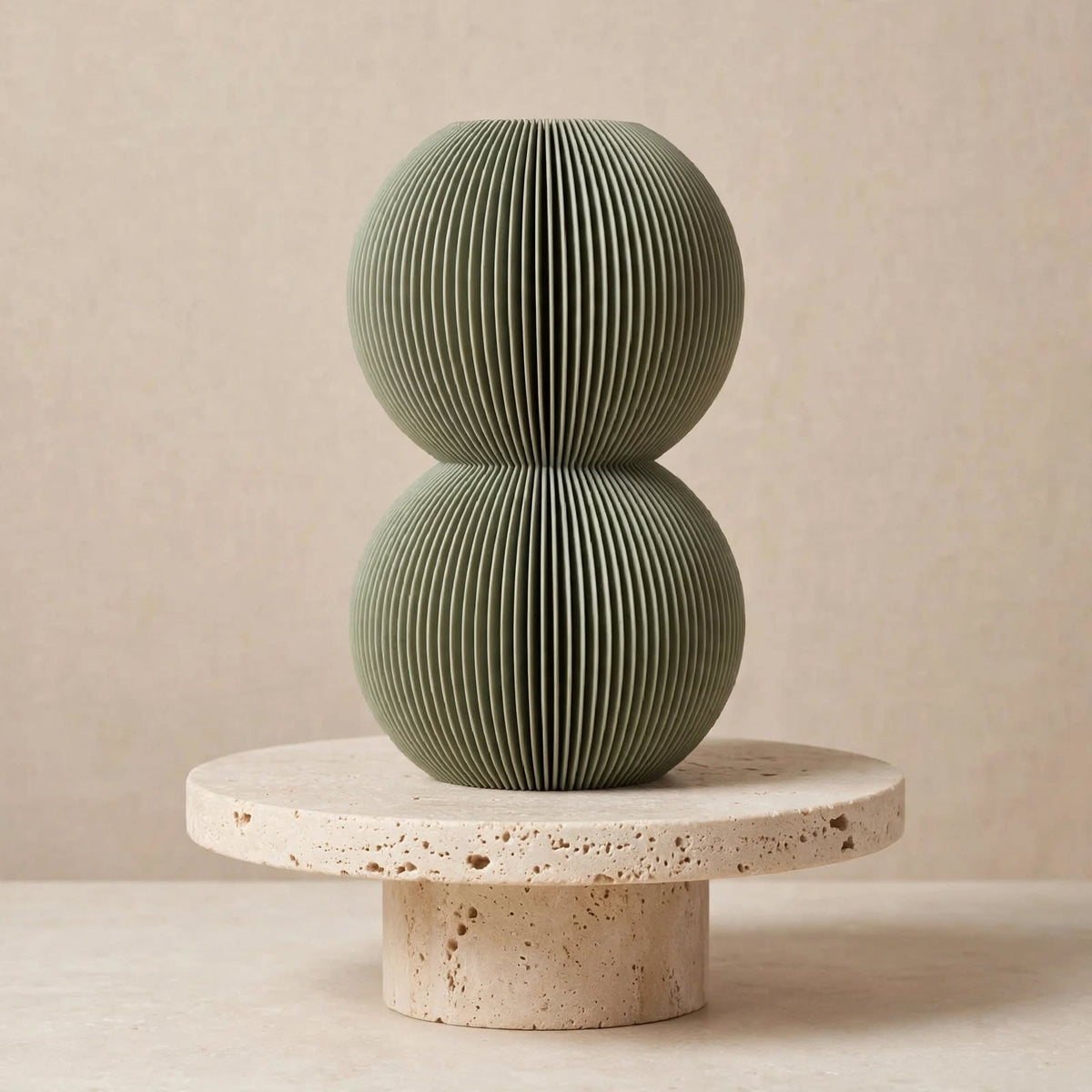 Muted green double bubble vase on a round stone pedestal against a beige background