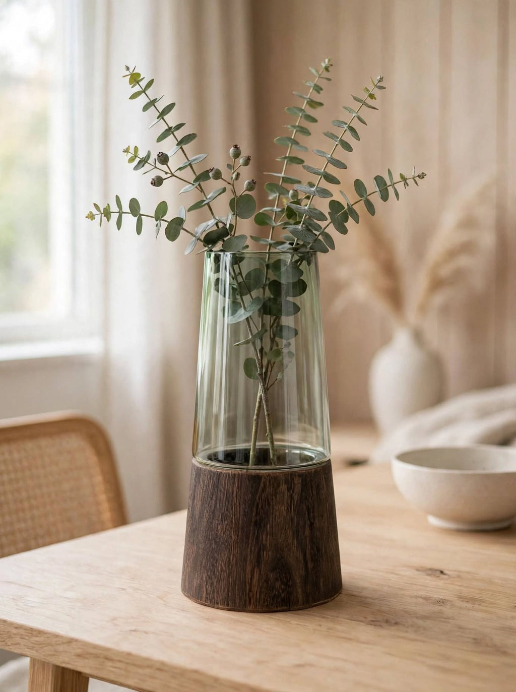 Smoky green glass vase on wooden base styled with eucalyptus on a wooden table