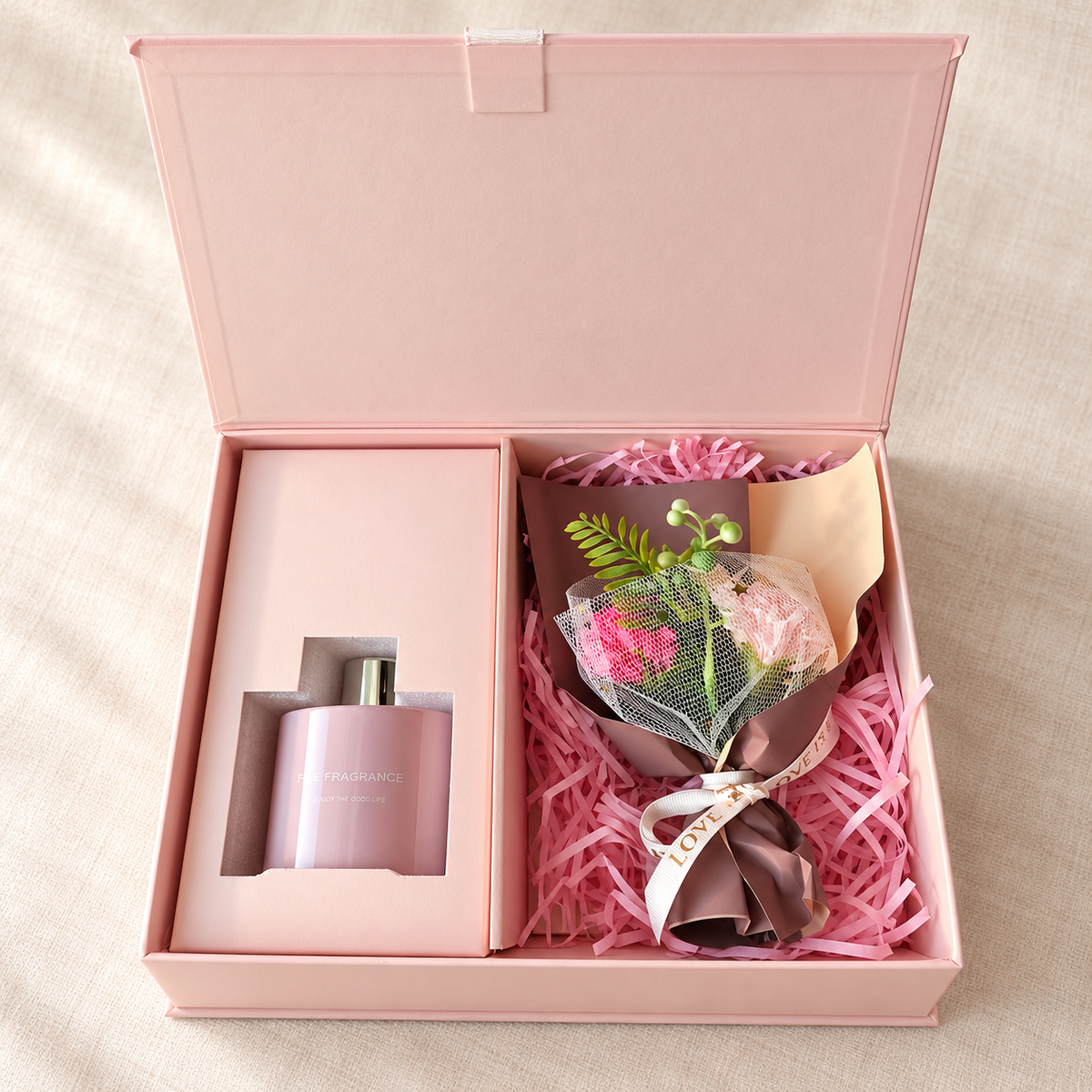 Reed diffuser gift set with bouquet: open pink gift box with home fragrance diffuser and pink flower bouquet on pink shredded paper