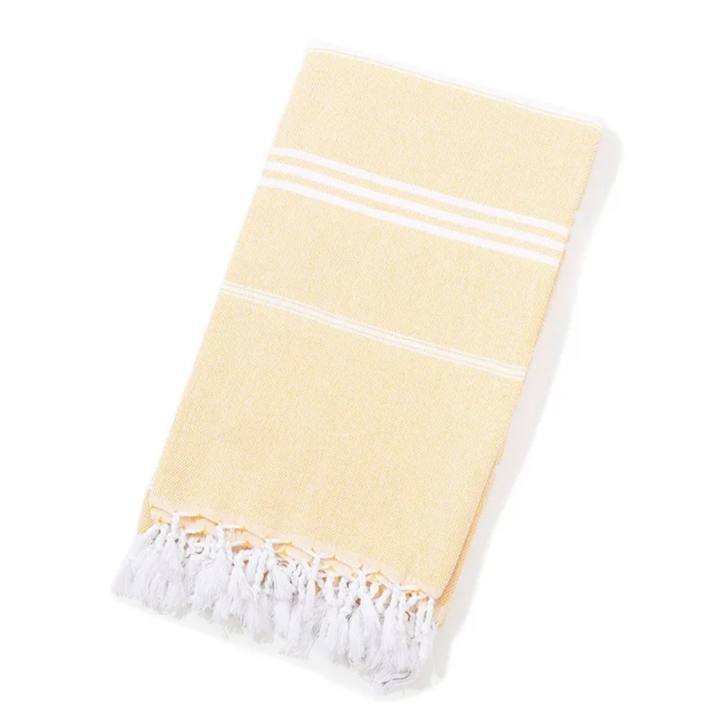 Folded pale yellow Turkish beach towel with white stripes and tassels on white background