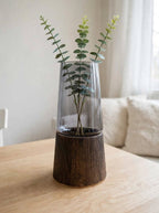 Light smoky grey glass vase on wooden base styled with eucalyptus