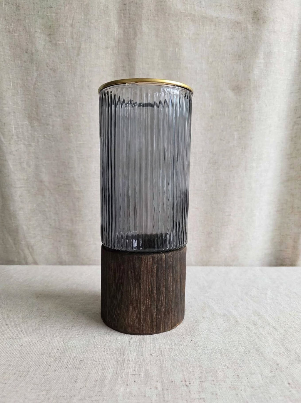 Smoky ribbed glass vase with gold rim on a wooden base, studio shot