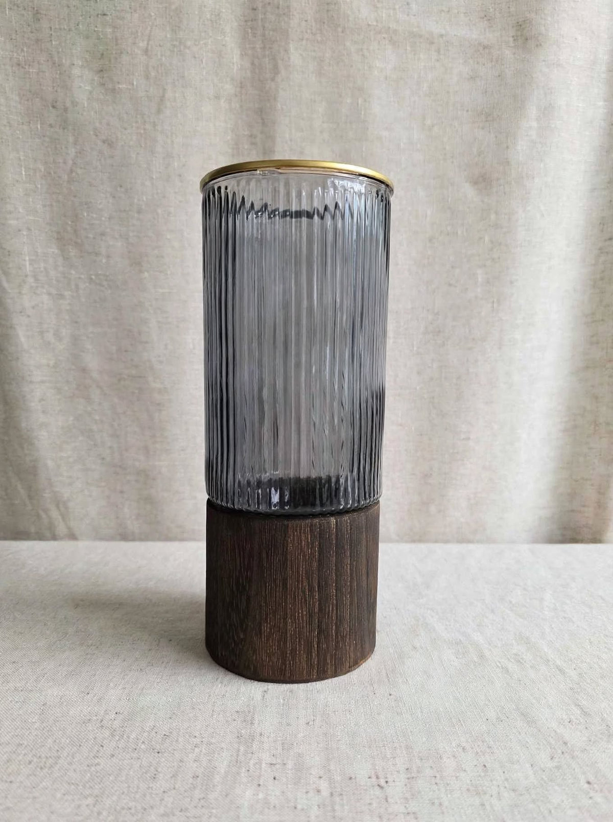 Smoky ribbed glass vase with gold rim on a wooden base, studio shot