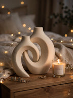 Matte white interlocking vases styled on a wooden nightstand with a lit candle and fairy lights
