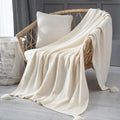 Beige knitted blanket draped over a wicker chair with a neutral background