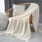 Beige knitted blanket draped over a wicker chair with a neutral background