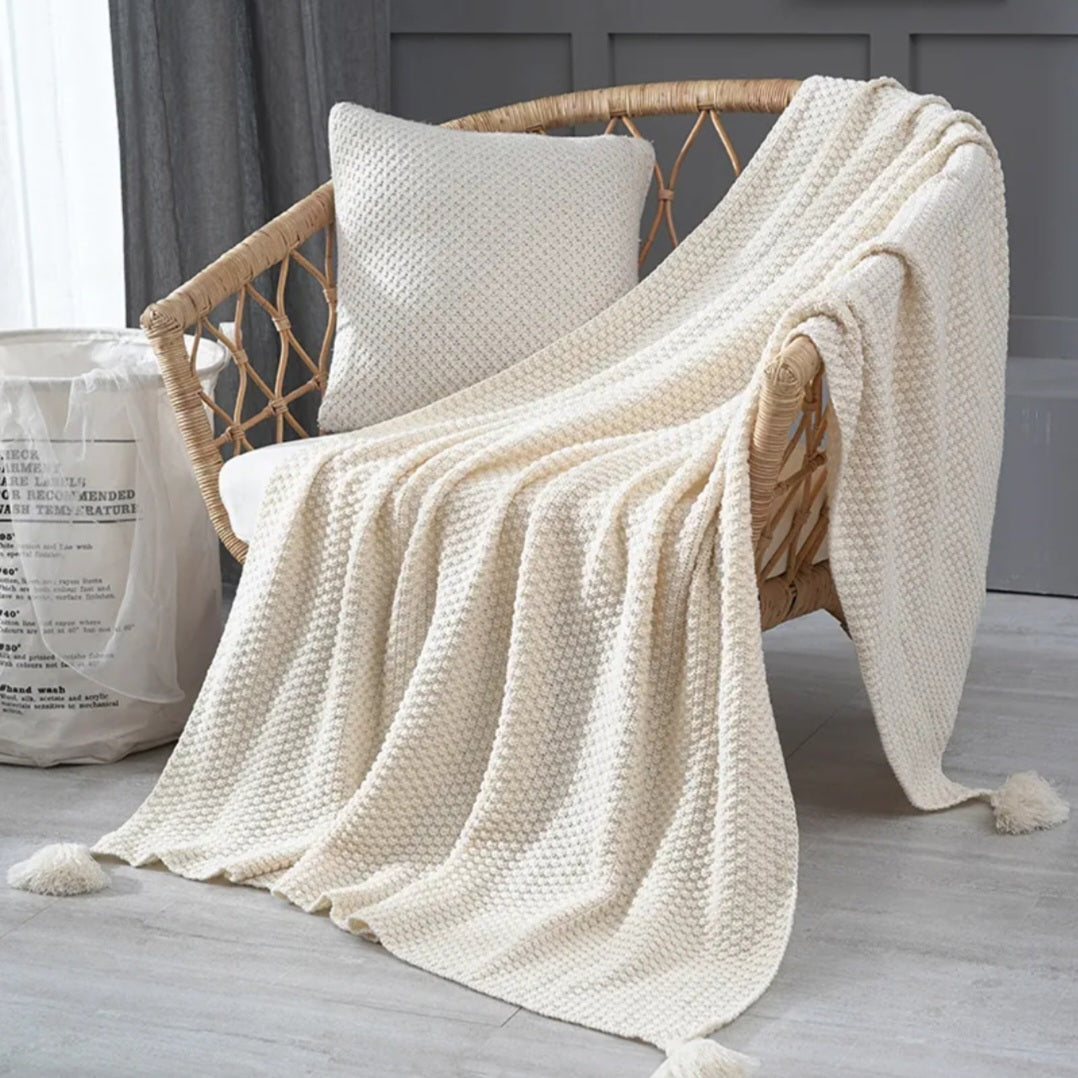 Beige knitted blanket draped over a wicker chair with a neutral background
