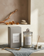 Aroma Home Sandalwood Smoke Candle shown with its gray packaging box, a glass jar candle with a glass lid.