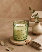 SOMA HOME Desert Bloom Scented Candle in a green textured glass jar with a single wick, styled on a wooden coaster with stacked books and a ceramic vase.
