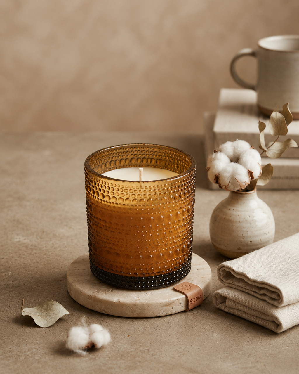 SOMA HOME Fresh Cotton Scented Candle in an amber textured glass jar, styled on a stone coaster with cotton bolls, folded linen, and a ceramic mug.