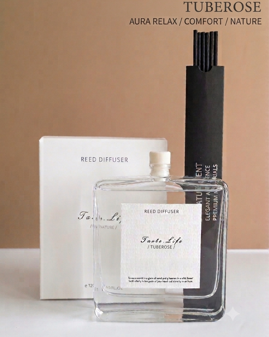 A clear glass reed diffuser bottle labeled 'Tuberose' with a white label, shown with a white box and a tall black reed holder against a warm beige background. Text at the top reads 'TUBEROSE AURA RELAX / COMFORT / NATURE'.