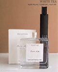 Aura Relax Comfort Nature Reed Diffuser in White Tea scent, featuring a clear glass bottle with a white label, a black reed holder, and its white packaging box against a warm beige background.